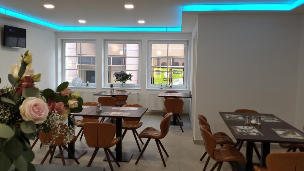 Moderne Lobby mit braunen Stühlen und Tischen, Blumenarrangement im Vordergrund, blauer LED-Beleuchtung und großen Fenstern., © TOMAS