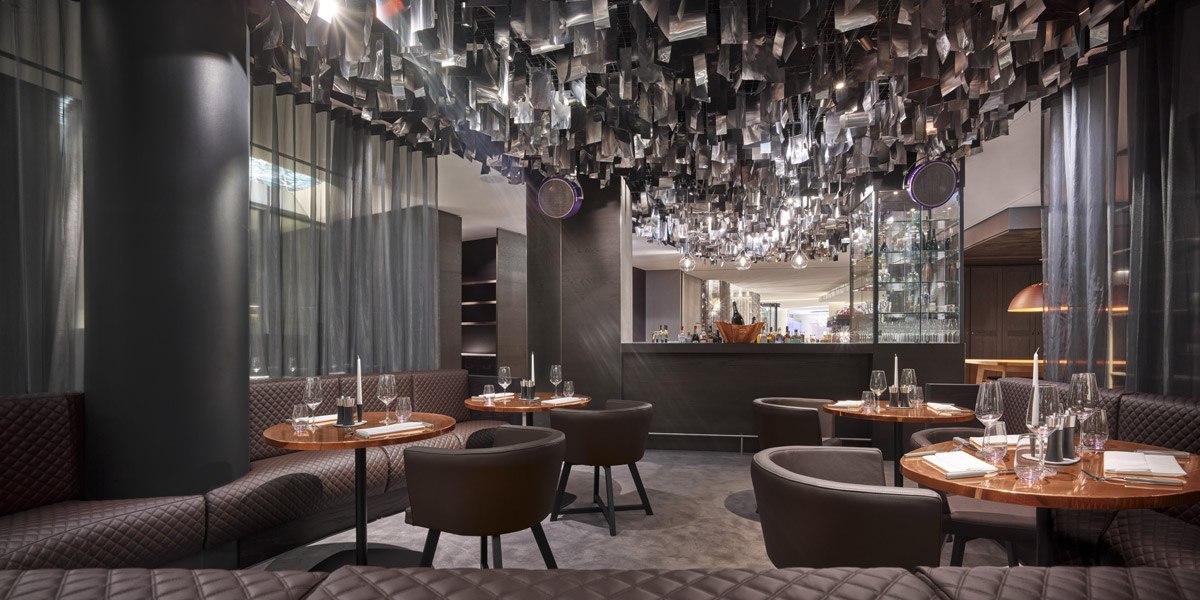 Elegant restaurant with round tables, upholstered chairs and a modern bar. The ceiling is adorned with decorative elements., © Jaz Hotel Stuttgart Elegant restaurant with round tables, upholstered chairs and a modern bar. The ceiling is adorned with decorative elements., © Jaz Hotel Stuttgart