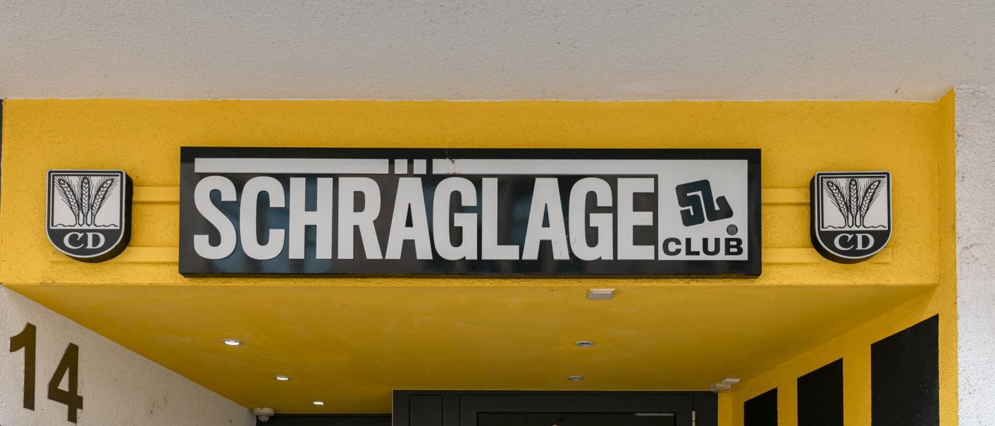 Eingang des Schräglage Clubs mit gelber Fassade und schwarzem Schild. Links und rechts sind CD-Logos mit Ähren abgebildet., © Stuttgart Marketing GmbH, Sarah Schmid
