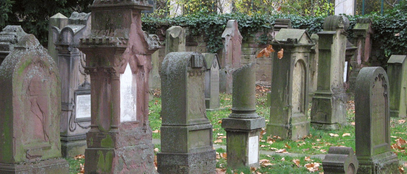 Alte, verwitterte Grabsteine auf dem Hoppenlau-Friedhof, umgeben von herbstlichem Laub und Efeu an einer Mauer., &copy; SMG