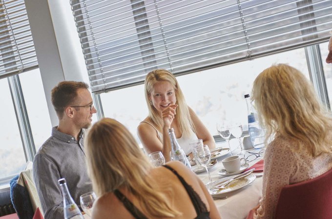 Four people are having breakfast at a table in a restaurant with large windows. They are chatting and enjoying their meal., © SWR Media Services GmbH / Fernsehturm Stuttgart Four people are having breakfast at a table in a restaurant with large windows. They are chatting and enjoying their meal., © SWR Media Services GmbH / Fernsehturm Stuttgart