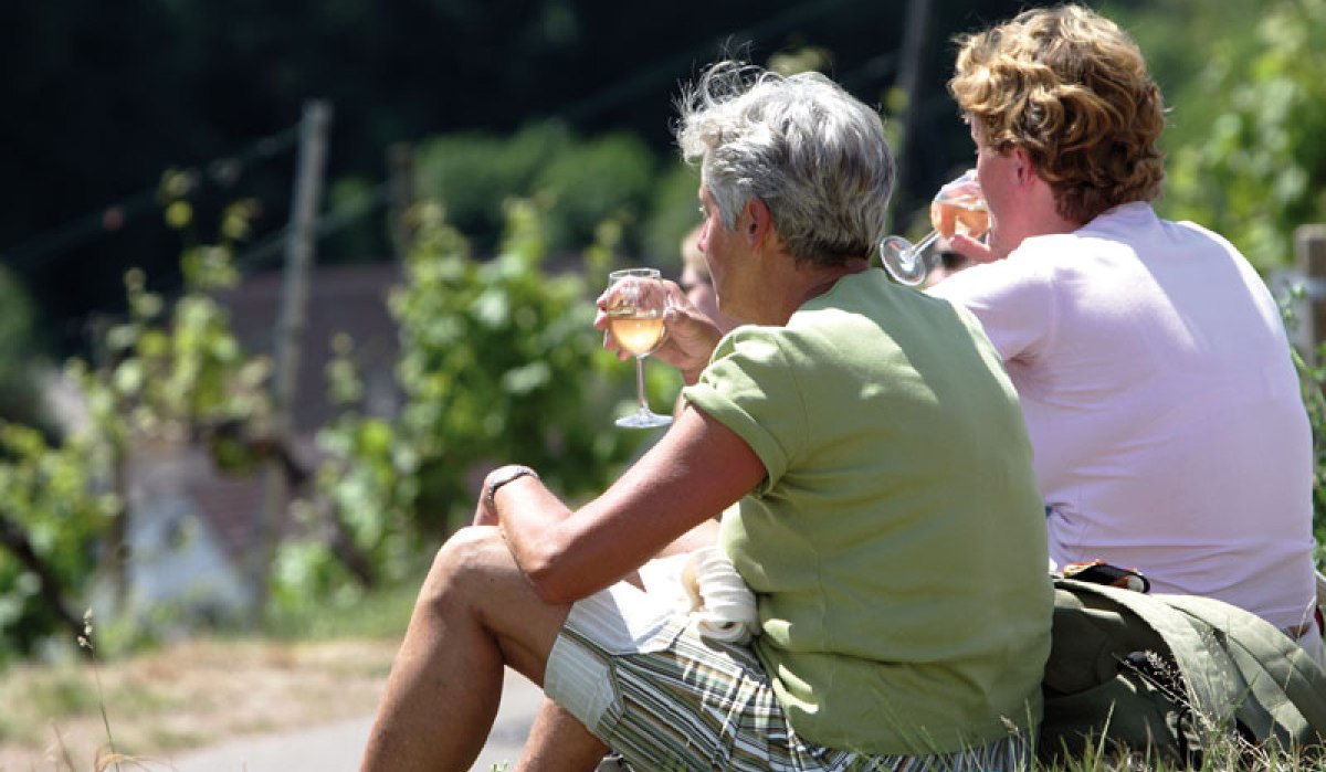 Zwei Personen sitzen im Gras und genießen ein Glas Wein auf einem Weinwanderweg. Im Hintergrund sind Weinreben zu sehen., © Stuttgart-Marketing GmbH