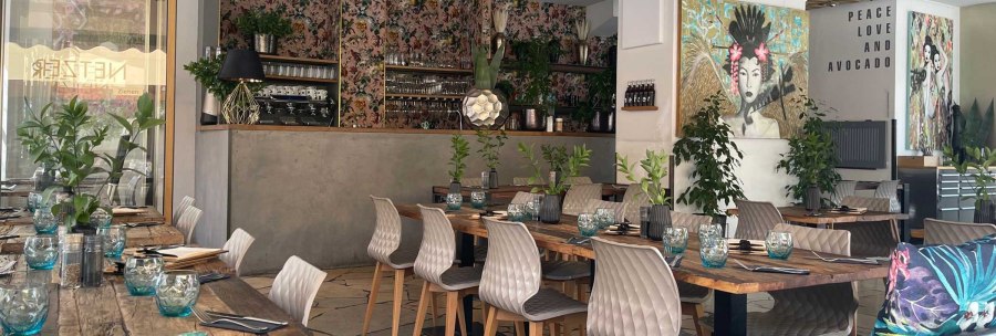 Stylishly furnished restaurant with wooden tables, modern chairs, plants and works of art. "Peace Love and Avocado" lettering on the wall., &copy; SMG