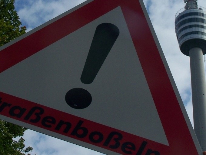 Ein Warnschild f&uuml;r Stra&szlig;enbo&szlig;eln mit einem Ausrufezeichen. Im Hintergrund ist ein Fernsehturm zu sehen., &copy; Cool-Tours StattReisen