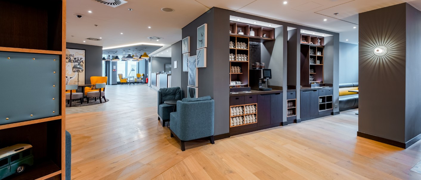Modern lounge with wooden floor, blue armchairs and yellow chairs. A coffee station and decorative pictures on the wall., © Premier Inn Modern lounge with wooden floor, blue armchairs and yellow chairs. A coffee station and decorative pictures on the wall., © Premier Inn