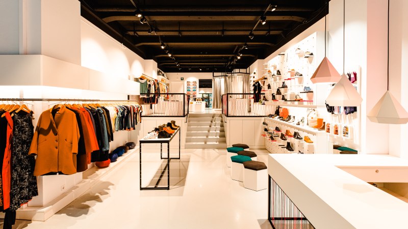 Ein modernes Bekleidungsgeschäft mit stilvoller Einrichtung, Kleidung an Kleiderstangen und Schuhen auf Regalen. Helle Beleuchtung und geometrische Lampen., © Elisa Mauruschat Ein modernes Bekleidungsgeschäft mit stilvoller Einrichtung, Kleidung an Kleiderstangen und Schuhen auf Regalen. Helle Beleuchtung und geometrische Lampen., © Elisa Mauruschat