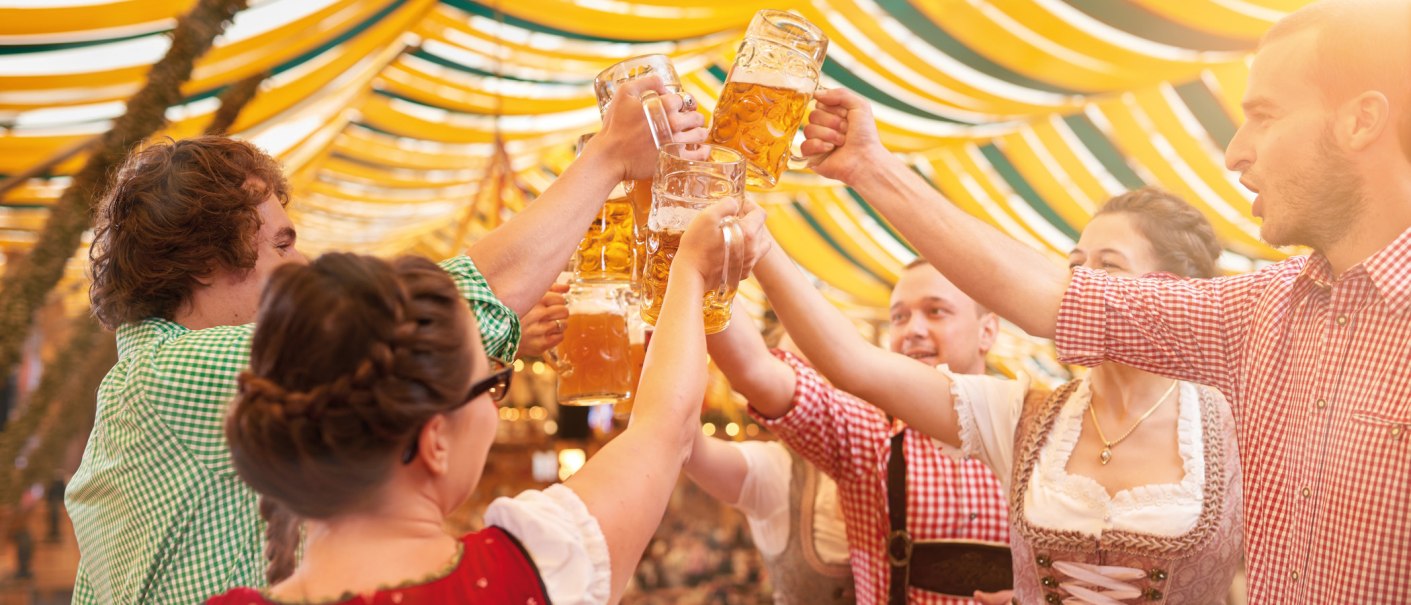 Group in traditional costume toasting with beer mugs in a festively decorated beer tent. A cheerful atmosphere under yellow and green fabric panels., © Stuttgart-Marketing GmbH, Jean-Claude Winkler Group in traditional costume toasting with beer mugs in a festively decorated beer tent. A cheerful atmosphere under yellow and green fabric panels., © Stuttgart-Marketing GmbH, Jean-Claude Winkler