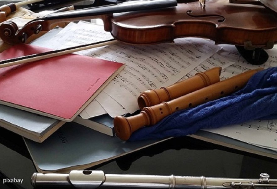 Geige, Blockflöten und Querflöte auf Notenblättern. Musikinstrumente liegen auf einem Tisch, umgeben von Partituren und einem roten Notenheft., © Pixabay