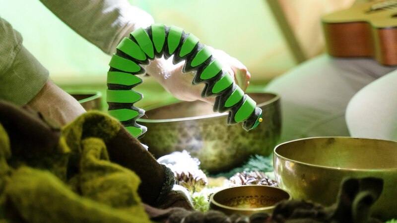 Eine Person hält ein grünes Spielzeug über mehrere Klangschalen. Im Hintergrund ist eine Gitarre zu sehen., © FITZ Das Theater animierter Formen