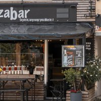 Au&szlig;enansicht einer Pizzabar mit Terrasse, Blumen und einem Werbeplakat. Ein Mann sitzt an einem Tisch. Die Markise ist schwarz., &copy; Stuttgart Marketing GmbH, Sarah Schmid