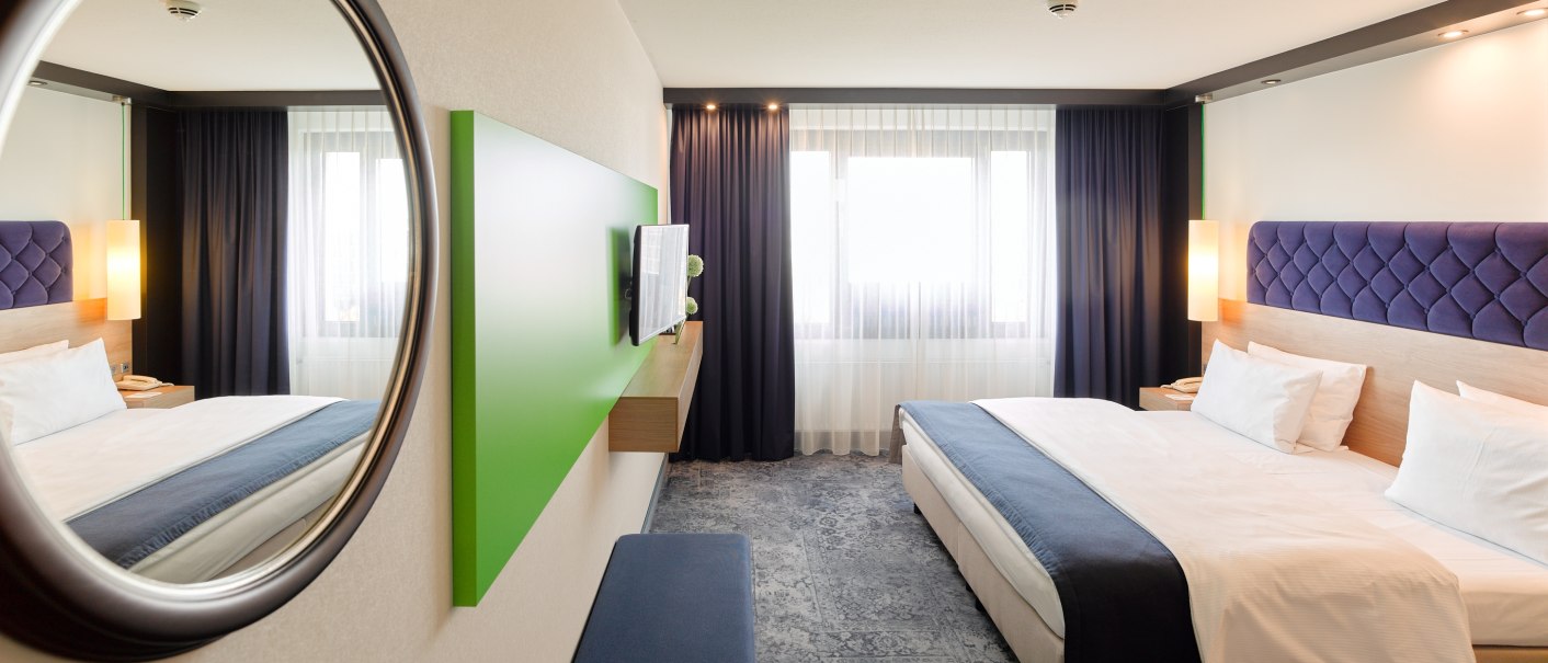 Modern hotel room with large bed, blue headboard, mirror, TV and large windows with curtains., © Holiday Inn Stuttgart Modern hotel room with large bed, blue headboard, mirror, TV and large windows with curtains., © Holiday Inn Stuttgart