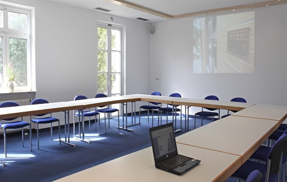 Empty conference room with U-shaped tables, blue chairs and a laptop. A projector shows a picture on the wall., © Hotel Neuwirtshaus Empty conference room with U-shaped tables, blue chairs and a laptop. A projector shows a picture on the wall., © Hotel Neuwirtshaus