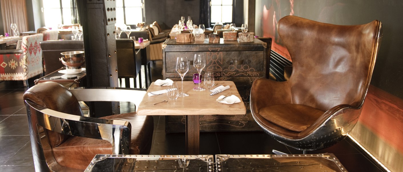 Ein stilvoll eingerichtetes Restaurant mit Ledersesseln und einem gedeckten Tisch. Im Hintergrund sind weitere Tische und Stühle zu sehen., © none Ein stilvoll eingerichtetes Restaurant mit Ledersesseln und einem gedeckten Tisch. Im Hintergrund sind weitere Tische und Stühle zu sehen., © none