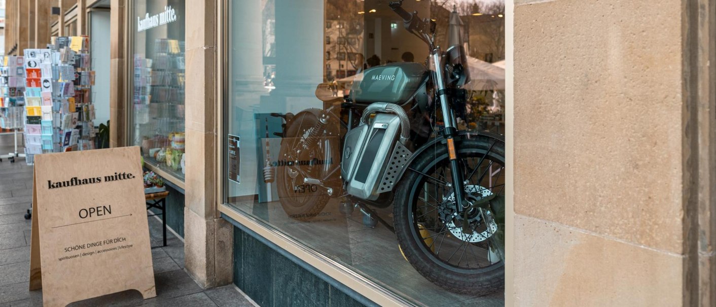 Schaufenster eines Kaufhauses mit einem Motorrad und einem Aufsteller mit der Aufschrift 'kaufhaus mitte'., © Stuttgart Marketing GmbH, Sarah Schmid Schaufenster eines Kaufhauses mit einem Motorrad und einem Aufsteller mit der Aufschrift 'kaufhaus mitte'., © Stuttgart Marketing GmbH, Sarah Schmid