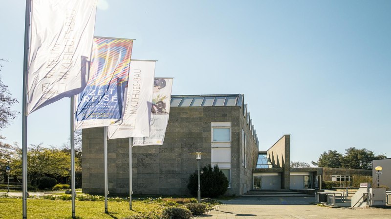 Das Museum Im Kleinhues-Bau in Kornwestheim, moderne Architektur mit mehreren Fahnen im Vordergrund, sonniger Tag., © SMG, Sarah Schmid Das Museum Im Kleinhues-Bau in Kornwestheim, moderne Architektur mit mehreren Fahnen im Vordergrund, sonniger Tag., © SMG, Sarah Schmid