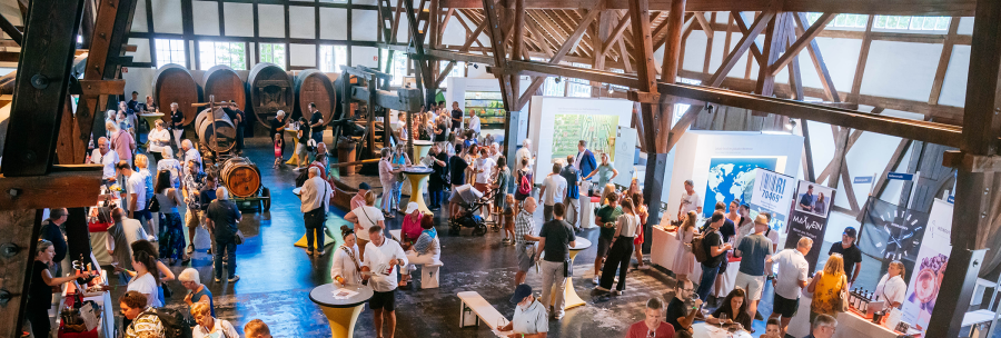 Weindegustation in Uhlbach: Viele Menschen probieren Wein in einer gro&szlig;en Halle mit Holzbalken und Weinf&auml;ssern. Es herrscht eine lebhafte Atmosph&auml;re., &copy; Stuttgart-Marketing GmbH, Thomas Niederm&uuml;ller