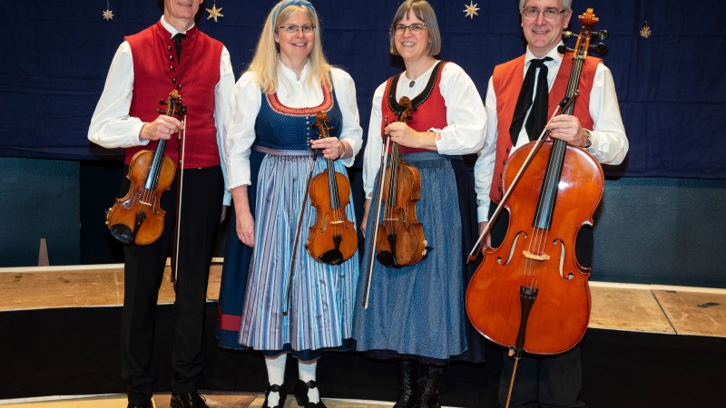 Four musicians in traditional dress holding string instruments. They stand in front of a blue background with star decorations., &copy; Peter Oehl