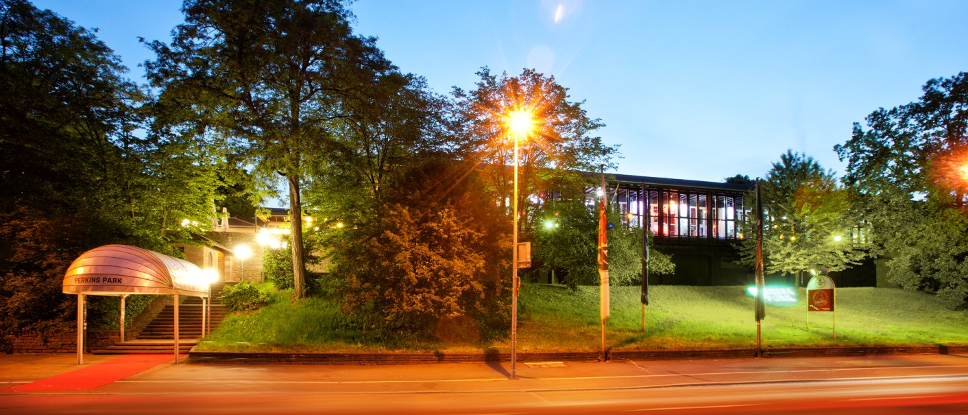 Eingang des Perkins Park bei Nacht, beleuchtet mit rotem Teppich. Im Hintergrund sind B&auml;ume und ein modernes Geb&auml;ude zu sehen., &copy; PerkinsPark