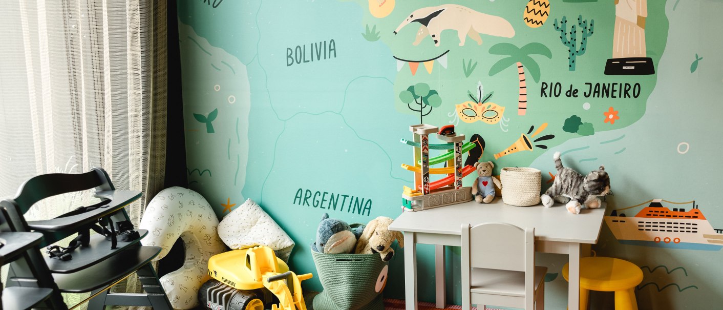 Ein Kinderzimmer mit einer bunten Wandkarte von Südamerika, Spielzeug, einem kleinen Tisch und Stühlen. Die Karte zeigt Länder wie Brasilien und Peru., © TOMAS