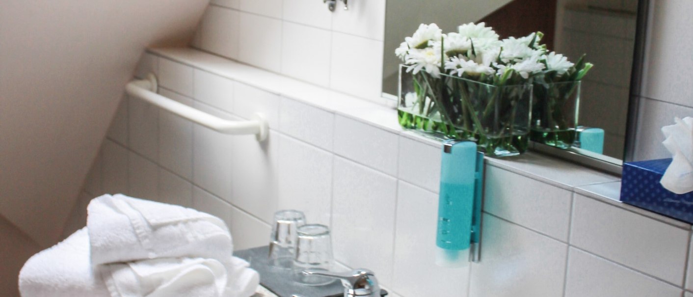 Ein Badezimmer mit Waschbecken, weißen Handtüchern, einem Spiegel, Blumen und einem Dachfenster., © Hotel Princess Ein Badezimmer mit Waschbecken, weißen Handtüchern, einem Spiegel, Blumen und einem Dachfenster., © Hotel Princess