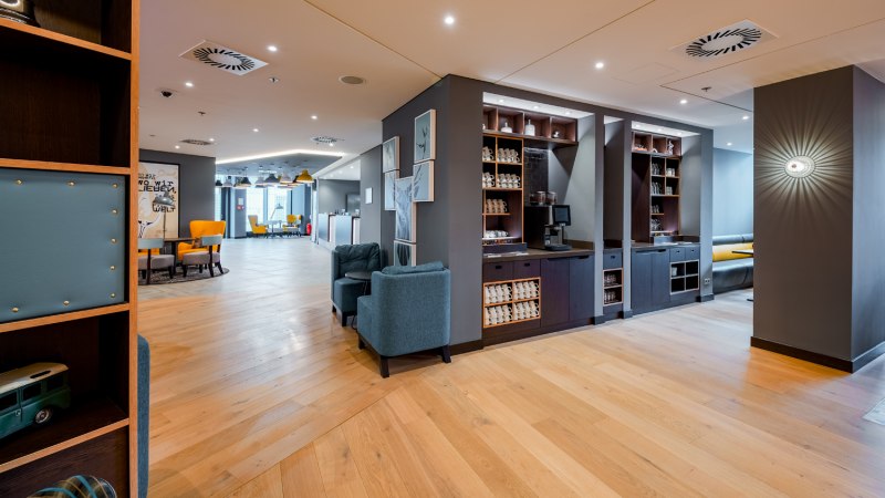 Modern lounge with wooden floor, blue armchairs and yellow chairs. A coffee station and decorative pictures on the wall., © Premier Inn