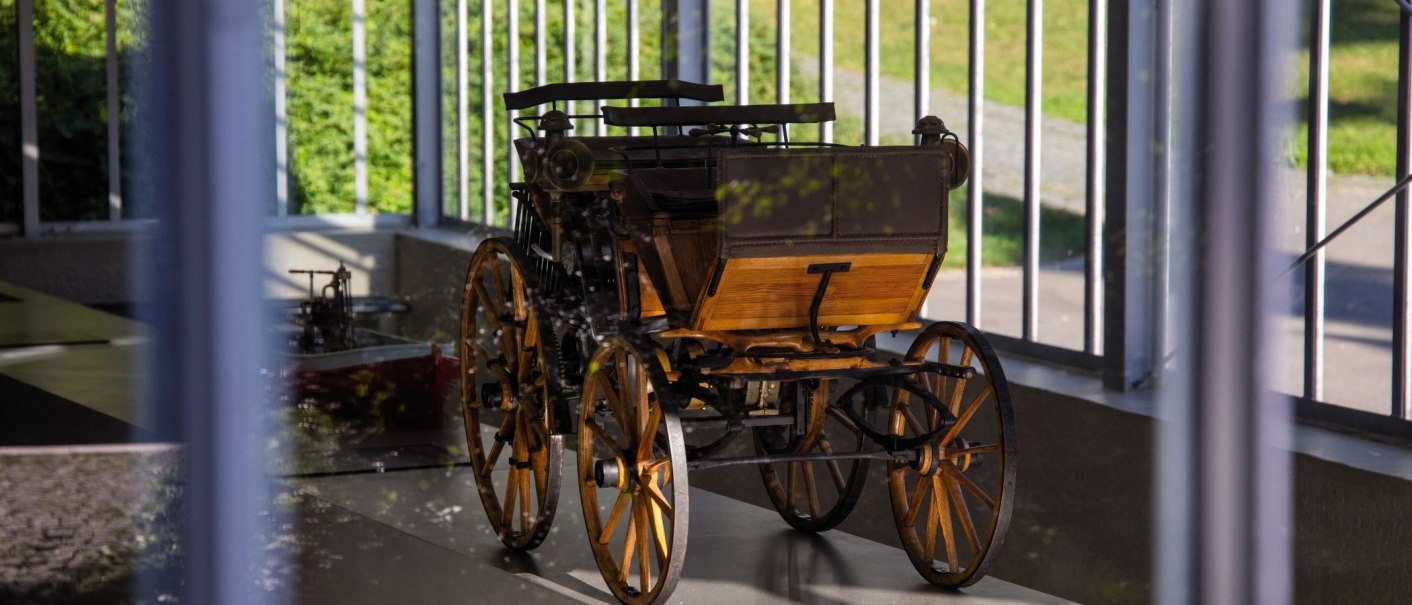 A historic vehicle with wooden wheels stands in a glass pavilion. Sunlight falls through the windows and illuminates the exhibit., © Stuttgart-Marketing GmbH Achim Mende