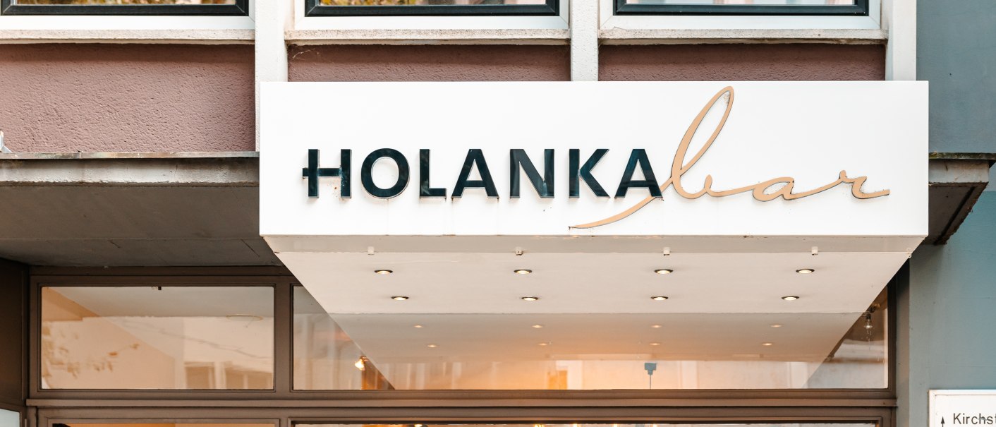 Eingang der Holanka Bar mit einem weißen Schild, auf dem der Name in schwarzer und goldener Schrift steht. Innenansicht mit Beleuchtung sichtbar., © SMG Stuttgart Marketing GmbH - Sarah Schmid