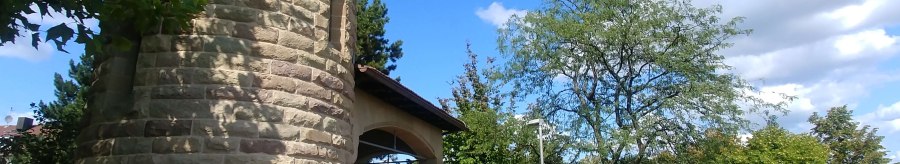 Runder Steinturm mit Zinnen, umgeben von B&auml;umen und blauem Himmel. Der Turm steht auf einer gepflasterten Fl&auml;che., &copy; SMG