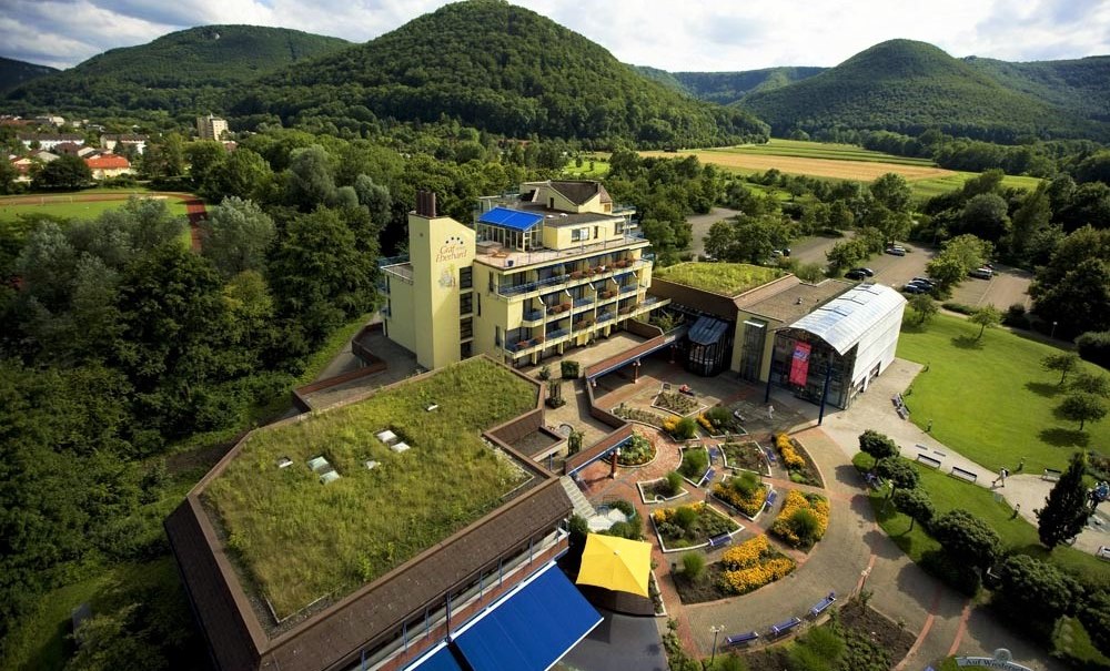 Luftaufnahme des Hotel Graf Eberhard mit begrüntem Dach, umgeben von grüner Landschaft und Hügeln im Hintergrund., © ©hotel-graf-eberhard.de