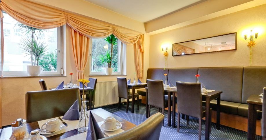 Ein gemütlicher Frühstücksraum mit gedeckten Tischen, Pflanzen auf der Fensterbank und eleganten Vorhängen. Ein Spiegel hängt an der Wand., © ARNOTEL GmbH