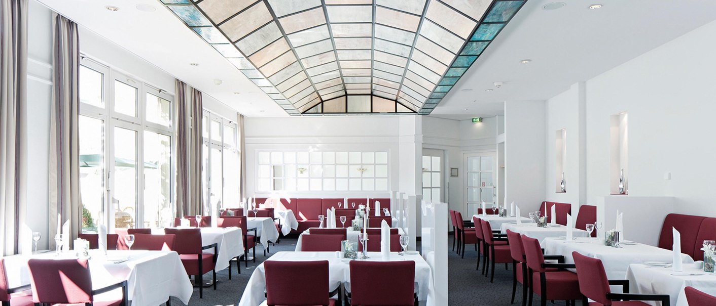 Elegantes Restaurant mit roten Stühlen, weißen Tischdecken und einem Glasdach. Helle Fensterfront und stilvolle Einrichtung., © Seminaris Hotel Bad Boll