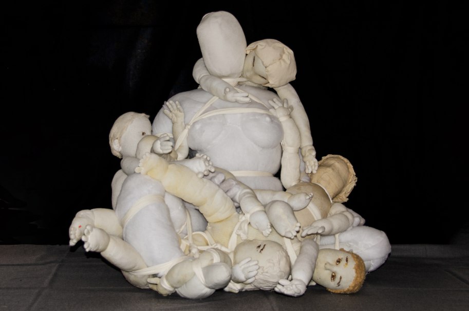 Eine ausdrucksstarke Stoffskulptur zeigt eine Frauengestalt, umgeben von mehreren festgebundenen Kindern. Die Figuren sind in hellen T&ouml;nen gehalten., &copy; Min Bark