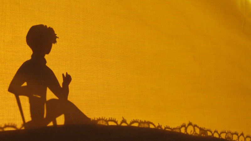 Ein Scherenschnitt zeigt ein Kind, das vor einem gelben Hintergrund sitzt. Die Silhouette ist detailliert und wirkt k&uuml;nstlerisch., &copy; Helen Pavel