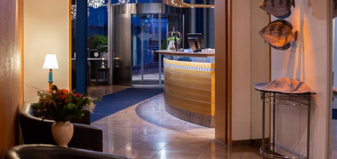 Elegant hotel lobby with reception desk, flower arrangement and decorative fish sculptures on the wall. The floor is made of shiny marble., © Kronen Hotel GmbH