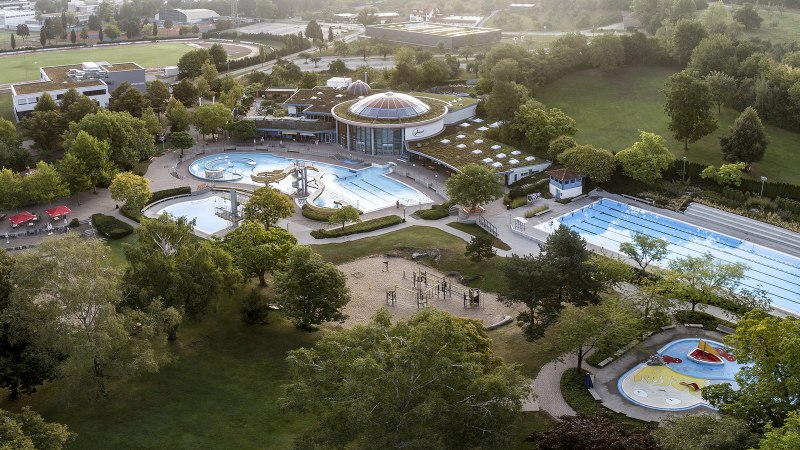 Luftaufnahme des Wunnebads in Winnenden: Schwimmbecken, Rutschen und grüne Umgebung. Sportplatz im Hintergrund., © Stadtwerke Winnenden GmbH