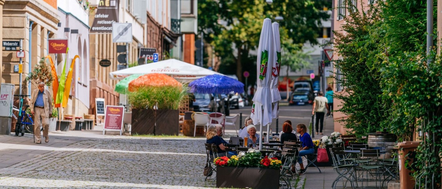 Straßenszene im Bohnenviertel mit Menschen, die an Tischen im Freien sitzen. Bunte Sonnenschirme und Pflanzen schmücken die Umgebung., © Thomas Niedermüller Straßenszene im Bohnenviertel mit Menschen, die an Tischen im Freien sitzen. Bunte Sonnenschirme und Pflanzen schmücken die Umgebung., © Thomas Niedermüller