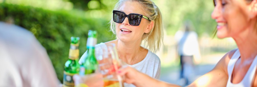 Drei Personen sto&szlig;en im Freien mit Getr&auml;nken an. Eine Frau tr&auml;gt eine Sonnenbrille und l&auml;chelt. Die Szene wirkt entspannt und sommerlich., &copy; Katzenbacher Hof