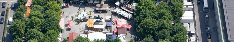 Aerial view of Karlsplatz in Stuttgart. Market stalls and colorful umbrellas are surrounded by trees. An equestrian statue stands in the center., &copy; Stuttgart-Marketing GmbH