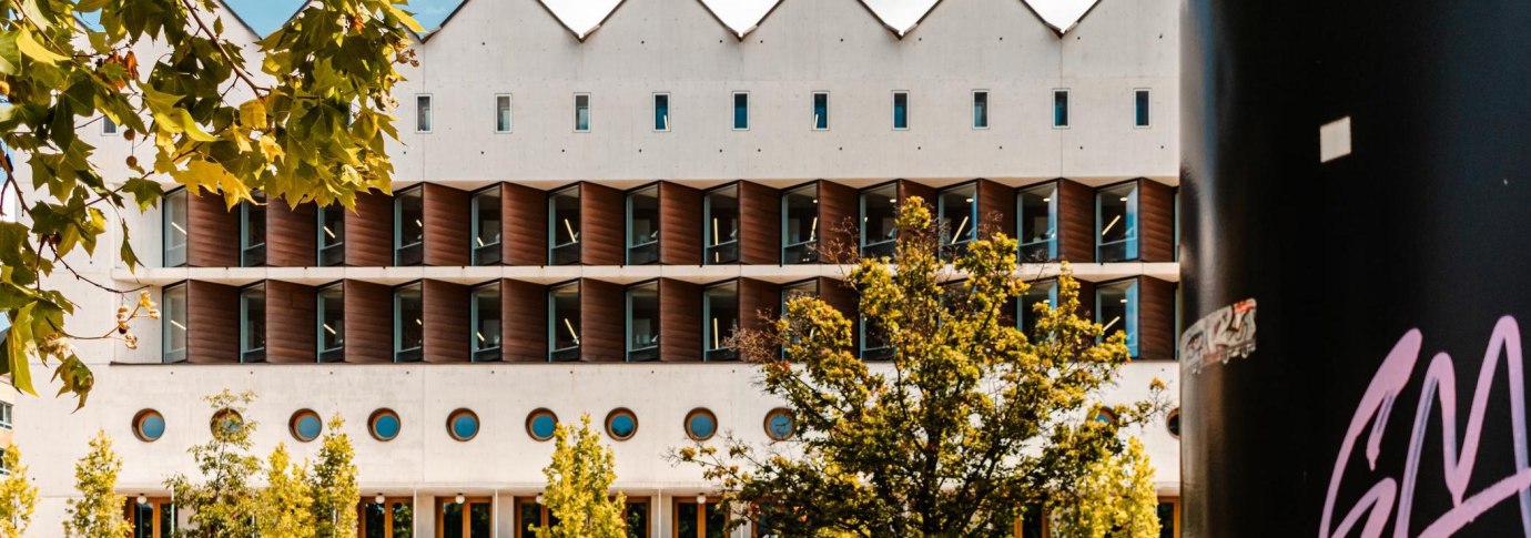 Moderne Bibliothek mit markanter geometrischer Fassade, umgeben von B&auml;umen. Ein schwarzer Pfeiler mit Graffiti ist rechts im Bild sichtbar., &copy; Stuttgart Marketing GmbH, Sarah Schmid