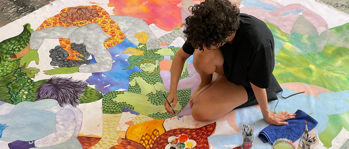 Ein K&uuml;nstler arbeitet an einem gro&szlig;en, bunten Kunstwerk auf dem Boden. Die Szene zeigt lebendige Farben und fantasievolle Figuren., &copy; Nadira Husain