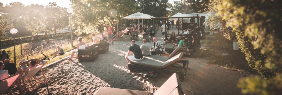 Menschen entspannen an einem sonnigen Stadtstrand in Stuttgart. Liegestühle und Sonnenschirme bieten eine gemütliche Atmosphäre im Sand., © Classic Rock Café Gastronomie- Betriebs GmbH