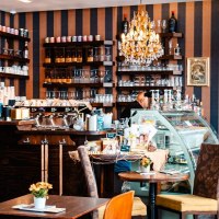 Gemütliches Kaffeehaus mit Kronleuchter, Regalen voller Produkte und einer Theke mit Kaffeemaschine. Tische mit Blumen dekoriert., © Stuttgart-Marketing GmbH, Sarah Schmid Gemütliches Kaffeehaus mit Kronleuchter, Regalen voller Produkte und einer Theke mit Kaffeemaschine. Tische mit Blumen dekoriert., © Stuttgart-Marketing GmbH, Sarah Schmid