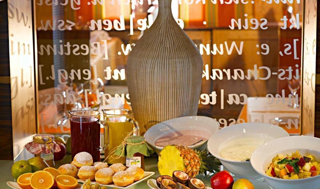 A breakfast buffet with fresh fruit, pastries, yogurt and juices. In the background, a large vase and decorative writing on the wall., © Nödinger Gastro GmbH