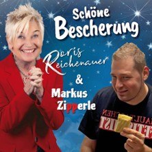 Zwei Personen vor einem blauen Hintergrund mit Sternen. Eine Frau in rotem Blazer lächelt, ein Mann hält ein Eis in der Hand. Text: Schöne Bescherung, Doris Reichenauer & Markus Zipperle., © links im Bild