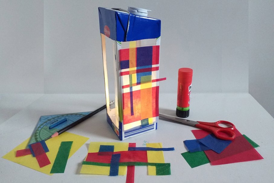 Selbstgemachte Laterne aus Milchkarton mit buntem Transparentpapier, umgeben von Schere, Kleber und Geodreieck auf einem Tisch., © StadtPalais Selbstgemachte Laterne aus Milchkarton mit buntem Transparentpapier, umgeben von Schere, Kleber und Geodreieck auf einem Tisch., © StadtPalais