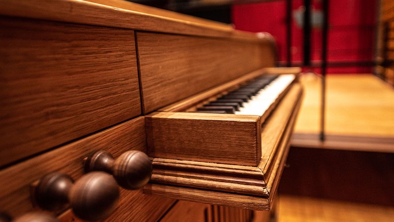 Nahaufnahme einer hölzernen Orgel mit sichtbaren Tasten und Knöpfen, im Hintergrund eine Bühne mit rotem Vorhang., © Staatliche Hochschule für Musik und Darstellende Kunst Nahaufnahme einer hölzernen Orgel mit sichtbaren Tasten und Knöpfen, im Hintergrund eine Bühne mit rotem Vorhang., © Staatliche Hochschule für Musik und Darstellende Kunst