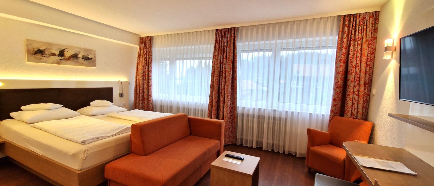 A modern hotel room with a double bed, an orange sofa, an armchair, a table, and a TV. Large windows with curtains., © TOMAS A modern hotel room with a double bed, an orange sofa, an armchair, a table, and a TV. Large windows with curtains., © TOMAS