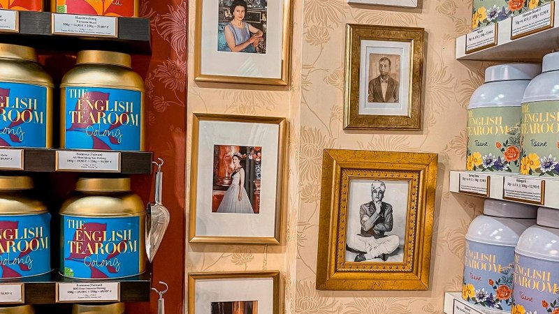 Regale mit Teedosen von 'The English Tearoom' und gerahmte Fotos an einer dekorativen Wand., © Tea Room, Stuttgart