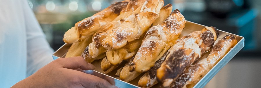 A person presents a tray of golden-brown, freshly baked pastry bars in a café., © Café Justus, Stuttgart