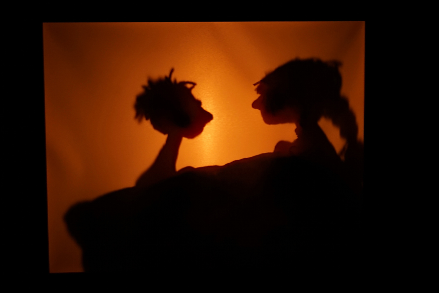 Zwei Schattensilhouetten von Figuren, die sich gegenüberstehen, vor einem warmen, orangefarbenen Hintergrund., © Theater in der Badewanne Zwei Schattensilhouetten von Figuren, die sich gegenüberstehen, vor einem warmen, orangefarbenen Hintergrund., © Theater in der Badewanne